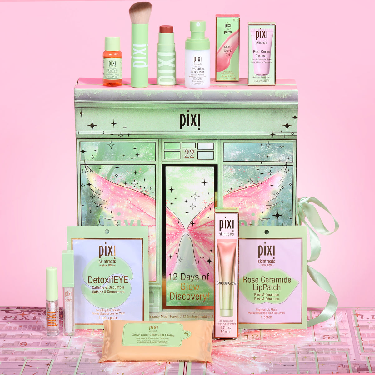 Pixi Beauty 12 Days of Discovery Beauty Advent Calenadr arranged on a pink background, featuring a pastel green gift box with wing artwork, assorted skincare and makeup items, and a pink ribbon.
