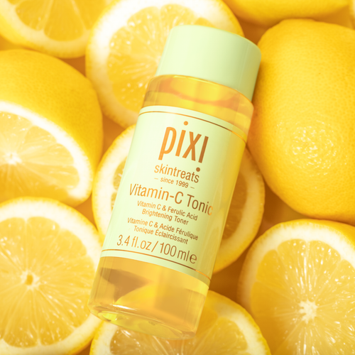 Pixi Skintreats Vitamin-C Tonic bottle with a light green cap, surrounded by fresh yellow lemon slices and whole lemons. view 1